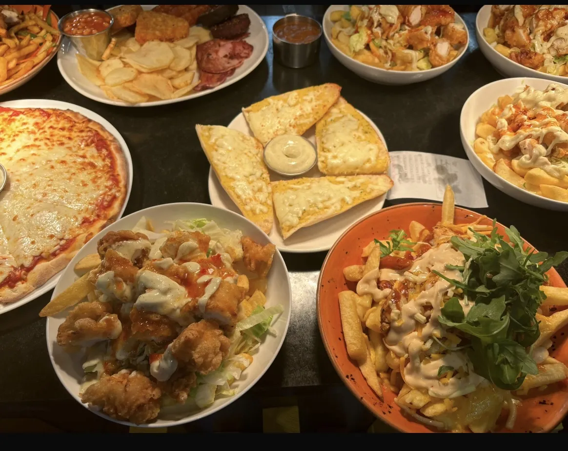 A table spread of pizza, wings, garlic bread and pasta